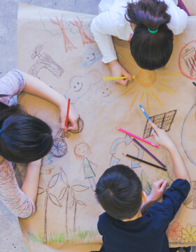three children drawing on a large piece of paper